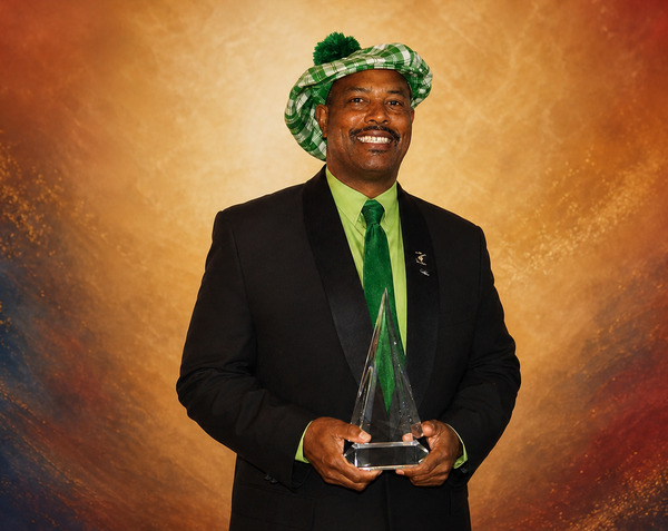 Award recipient wearing a green hat and holding a glass trophy
